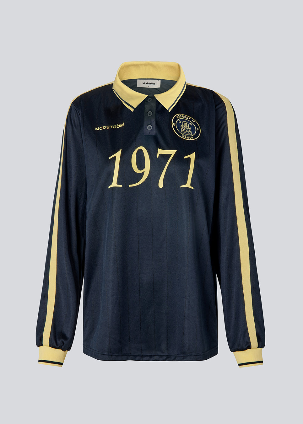 Fodbold jersey i mørkeblå med gule detaljer lavet i samarbejde med Brøndbys kvindehold. 1971 Polo har en løs pasform med stolpelukning og krave, samt lange ærmer med ribkant. Desuden har poloen Brøndby Womens og Modström logo på brystet.