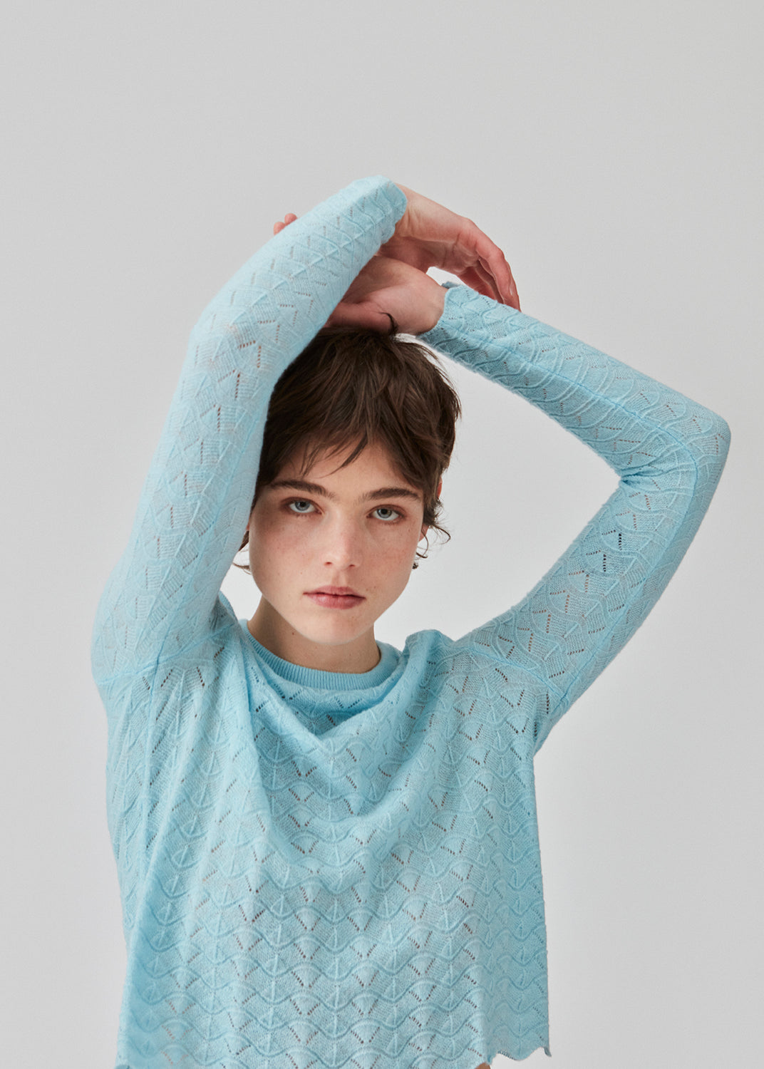 Strikket trøje i lyseblå med hulmønster i let kvalitet med uld. CordellMD short o-neck har en afslappet cropped pasform og lange ærmer med bølgede kanter. Modellen er 175 cm og har en størrelse S/36 på.