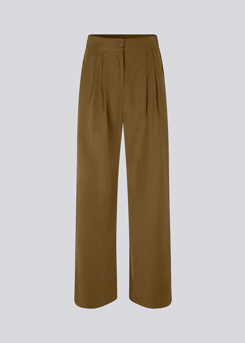 FanyaMD pants i brun har et herre-inspireret look med lige, brede ben, høj talje med lynlåsgylp og knap og elastik bagpå. Dobbeltlæg foran og sidelommer. Modellen er 175 cm og har en størrelse S/36 på.