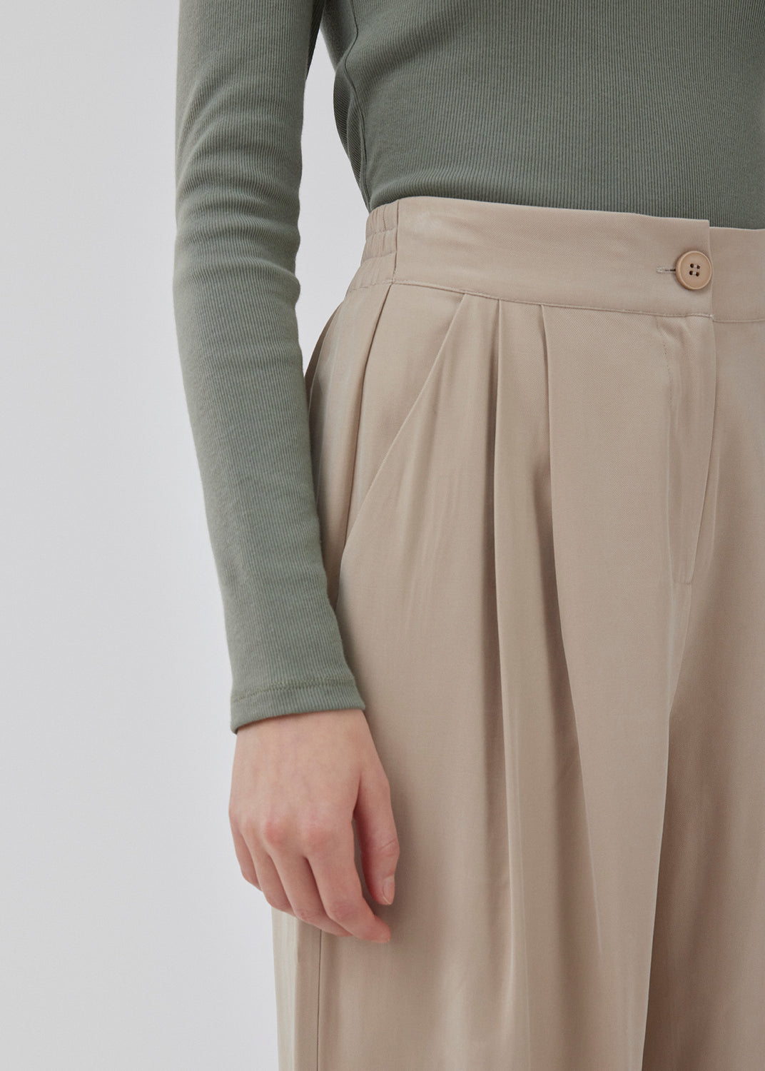 FanyaMD pants i lys beige har et herre-inspireret look med lige, brede ben, høj talje med lynlåsgylp og knap og elastik bagpå. Dobbeltlæg foran og sidelommer. Modellen er 175 cm og har en størrelse S/36 på.