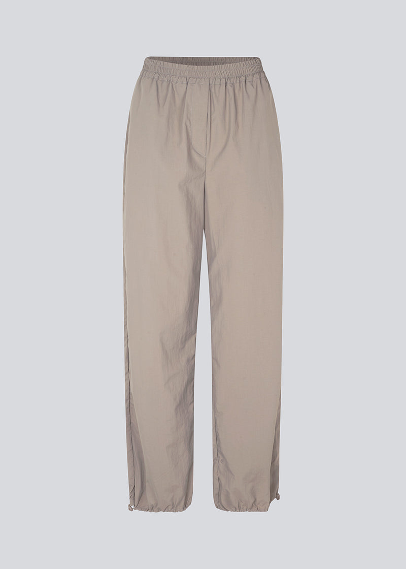 Faldskærmsbukser i beige i nylon med afslappet pasform. FumikoMD pants har almindelig talje med elastik, vide ben og elastisk snøre forneden. Modellen er 175 cm og har en størrelse S/36 på.