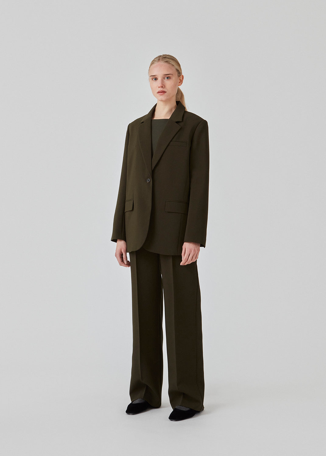 Gale blazer har et klassisk og elegant design i mørkegrøn, som kommer til udtryk i den flotte reverskrave og den lange pasform. Blazeren har knaplukning fortil og en brystlomme i venstre side. Modellen er 175 cm og har en størrelse S/36 på. Style blazeren med matchende bukser i samme farve: Gale pants.