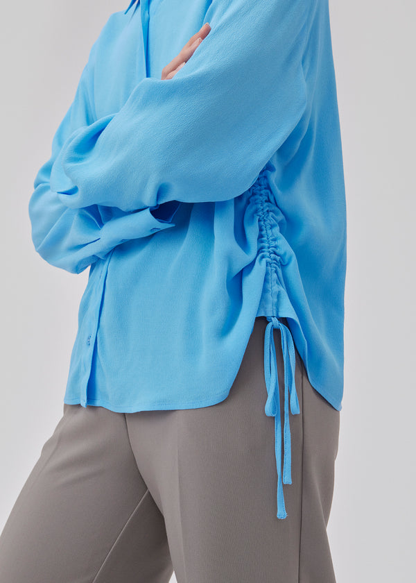 Oversize skjorte med krave, knaplukning fortil og brede ærmer med manchet. GelilaMD shirt har løbegang med bindebånd med rynkedetalje i den ene side. Modellen er 175 cm og har en størrelse S/36 på.