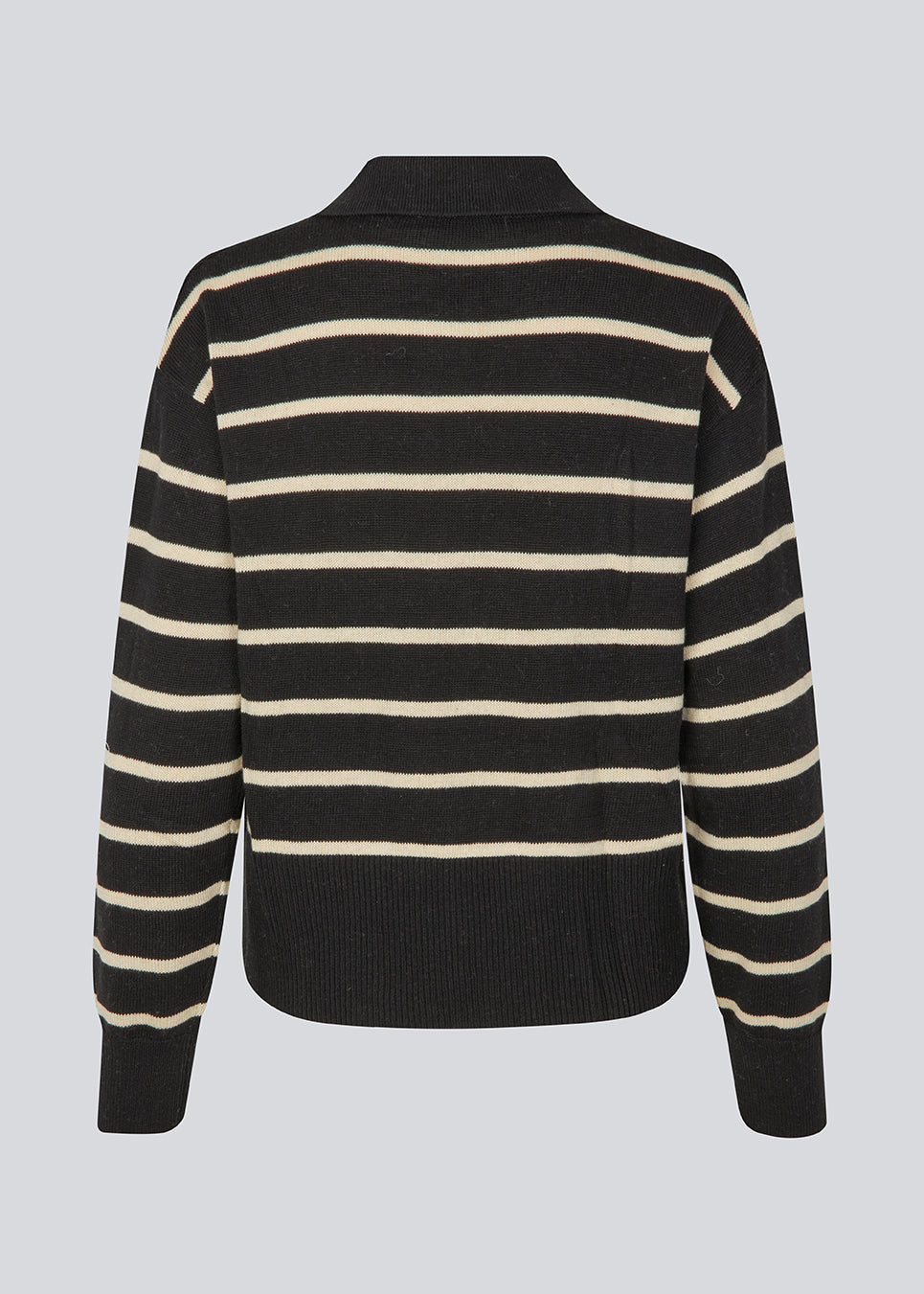 Blød strikket polo i sort med beige striber. MalvaMD stripe polo har en krave med stolpelukning. Modellen er 177 cm og har en str S/36 på. Strikken er lille i størrelsen, og kort.