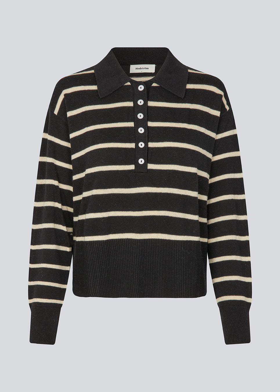 Blød strikket polo i sort med beige striber. MalvaMD stripe polo har en krave med stolpelukning. Modellen er 177 cm og har en str S/36 på. Strikken er lille i størrelsen, og kort.