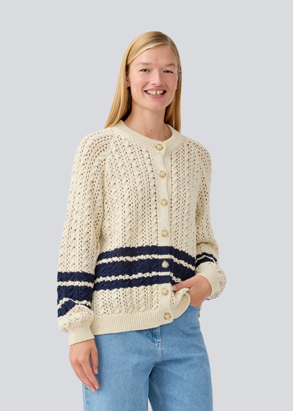 Løs strikket cardigan i beige med mørkeblå striber i kabel strik. MetteMD cardigan er let gennemsigtig, har løse ærmer og en knappelukning fortil. Modellen er 177 cm og har en str. S/36 på.