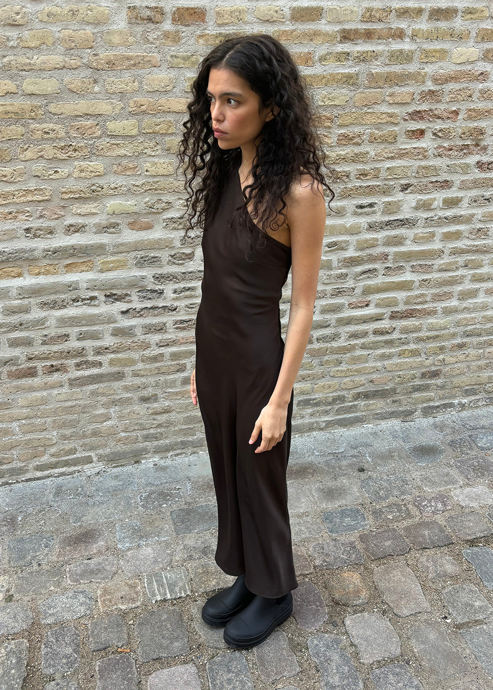 Vores populære Narcissamd dress er nu endelig kommet i en flot mørkebrun.
Mørkebrun lang one shoulder kjole i satin. NarcissaMD dress er en maxi dress med en åben ryg med smukke detaljer og en usynlig lynlås i siden.