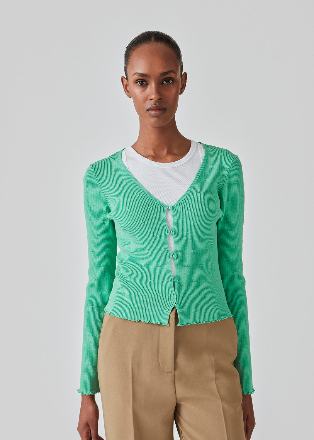 Tætsiddende, let cropped cardigan i grøn med knaplukning foran. DorisMD cardigan har en dybrund halsudskæring, lange ærmer og bølgekanter i bund og ved manchet. Modellen er 177 cm og har en størrelse S/36 på.