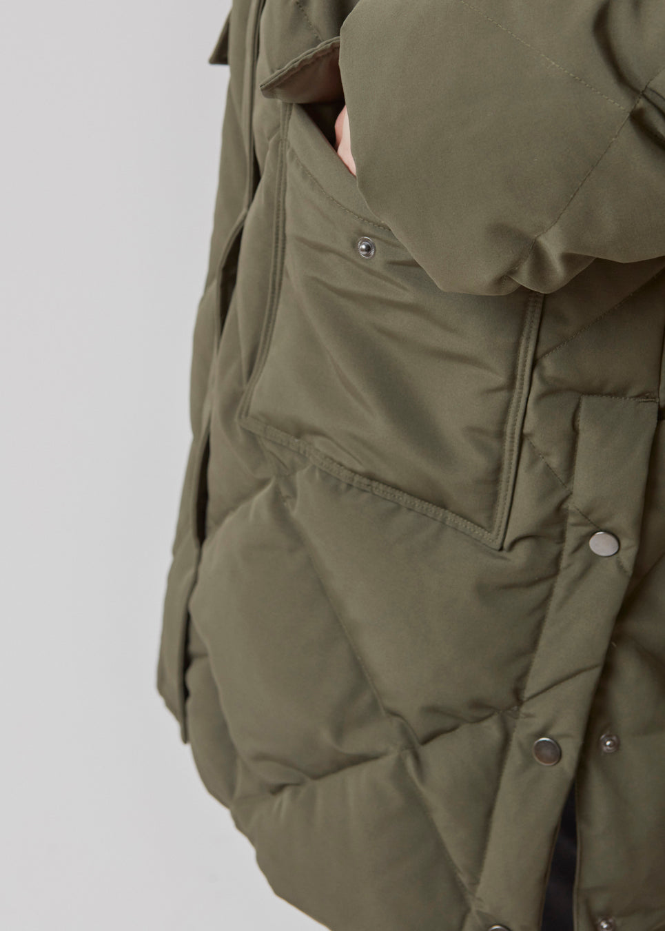 Quiltet jakke med fyld af duni grøn. ScarlettMD jacket er en knælang jakke med høj opretstående krave, samt lynlås og vindslå med trykknapper. Jakken har to forlommer med flap og trykknap og elastik nederst på ærmerne. Modellen er 177 cm og har en størrelse S/36 på.