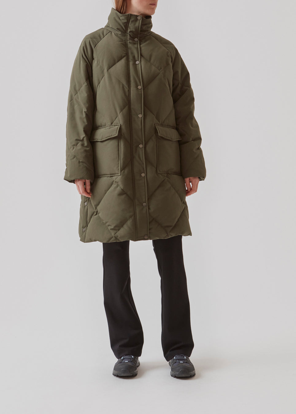 Quiltet jakke med fyld af duni grøn. ScarlettMD jacket er en knælang jakke med høj opretstående krave, samt lynlås og vindslå med trykknapper. Jakken har to forlommer med flap og trykknap og elastik nederst på ærmerne. Modellen er 177 cm og har en størrelse S/36 på.