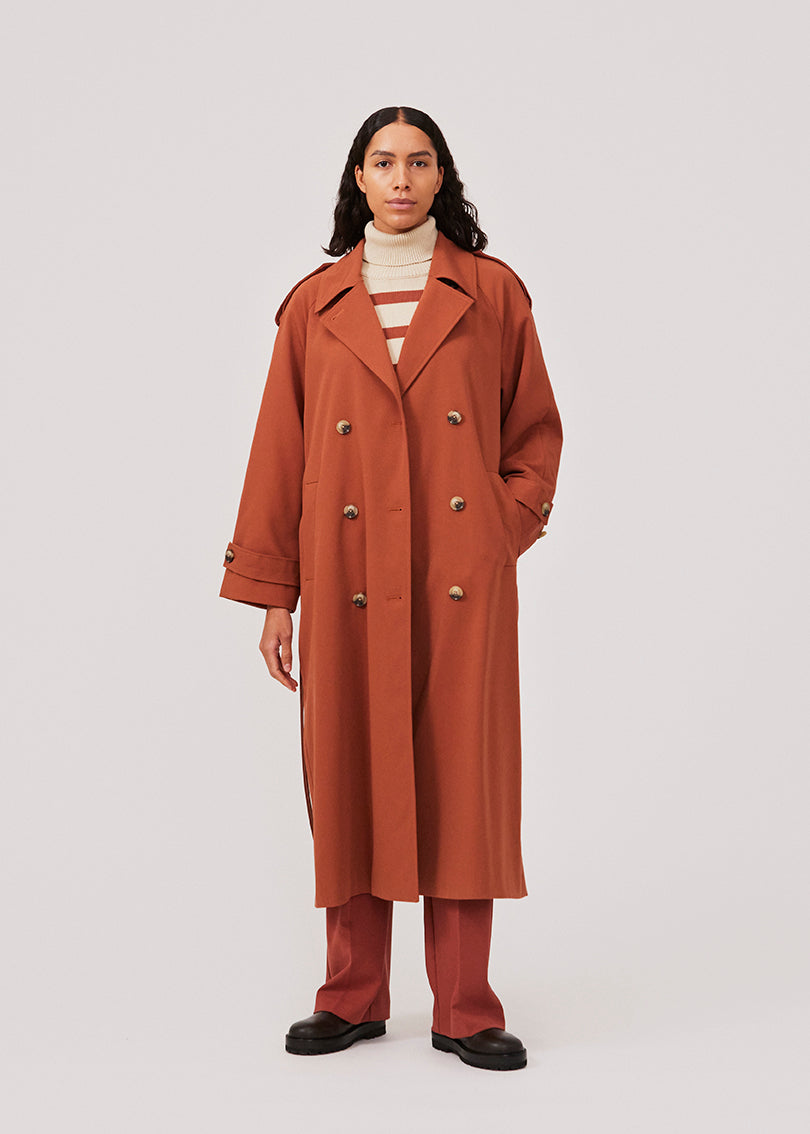 Oversized dobbeltradet trench coat i farven Maple med bindebånd i taljen. EvieMD jacket har lav skuldersøm og lange, brede ærmer. Med foer. Modellen er 175 cm og har en størrelse S/36 på.