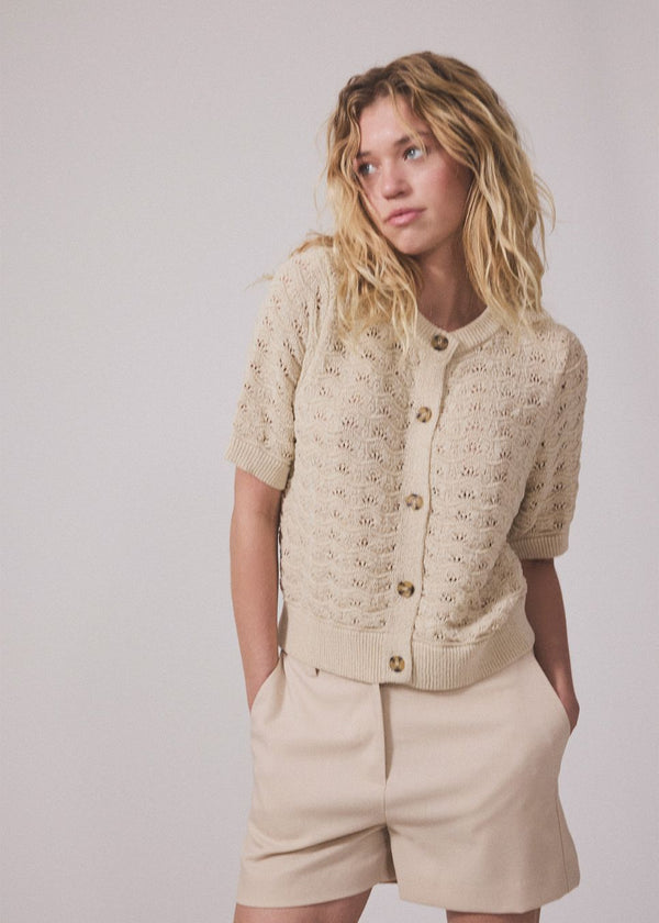 Kortærmet beige cardigan i strik med pointelle mønster. NeppoMD cardigan har en løs pasform og en knappelukning fortil.