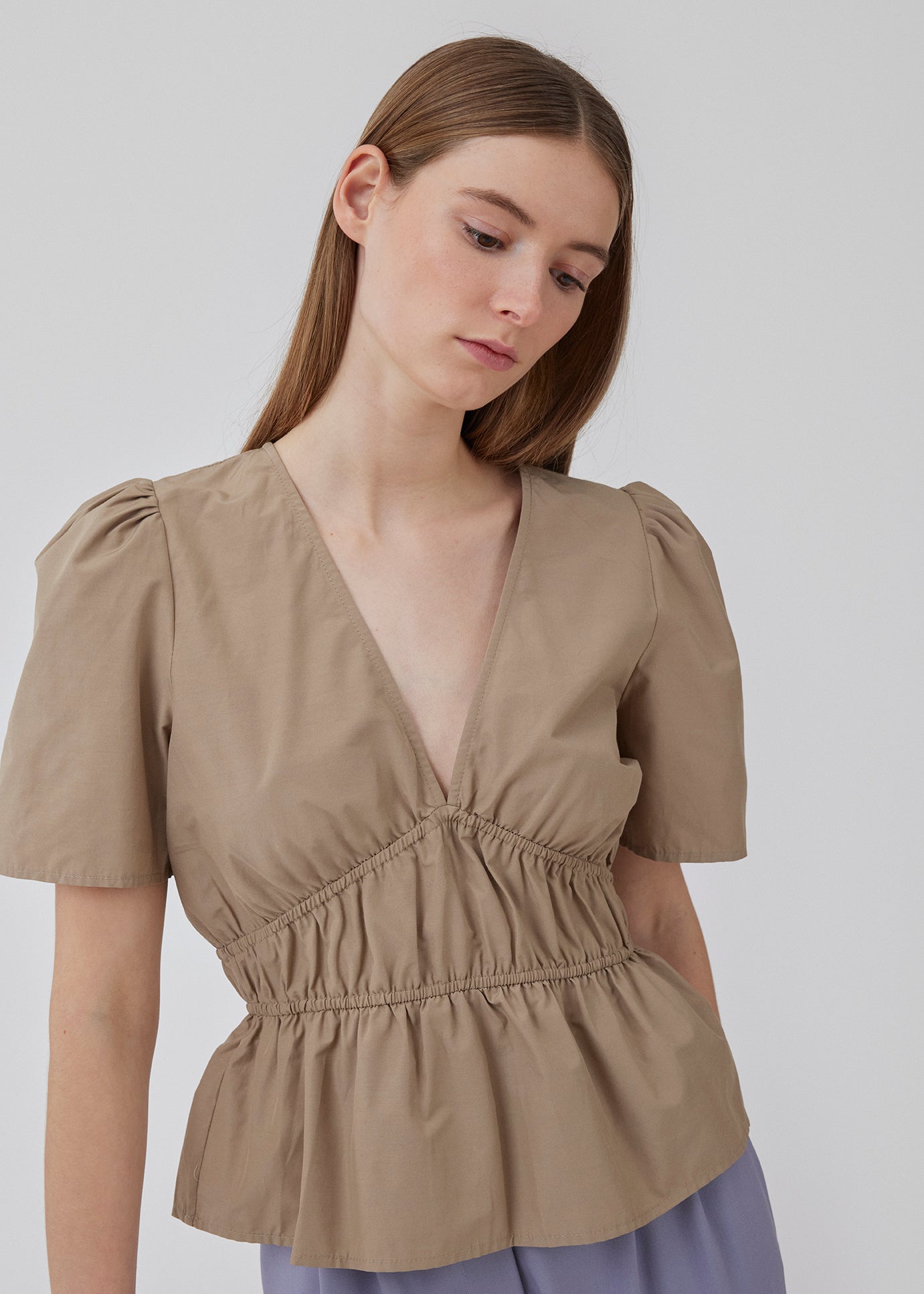 Top i beige i bomuldsblanding med korte ærmer med let puf og dyb v-udskæring i halsen. DeenMD top har flatterende rynkedetaljer under brystet og i taljen. Modellen er 177 cm og har en størrelse S/36 på.