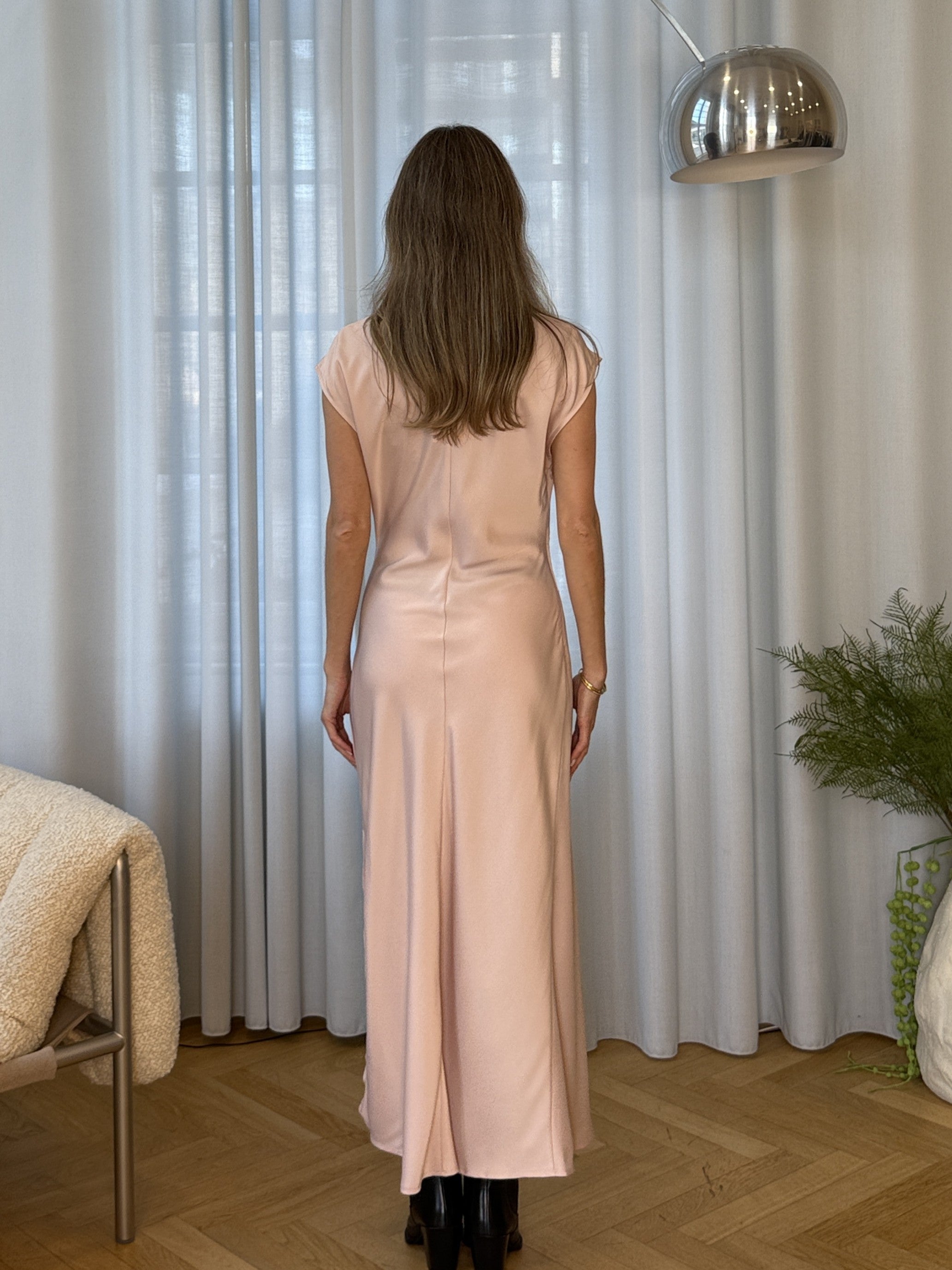 Lang ærmeløs kjole i lys rosa med rynkedetalje i satin. TailorMD dress har en høj hals, usynlig lynlås i ryggen og en slids i siden. Modellen er 175 cm og har en str S/36 på.