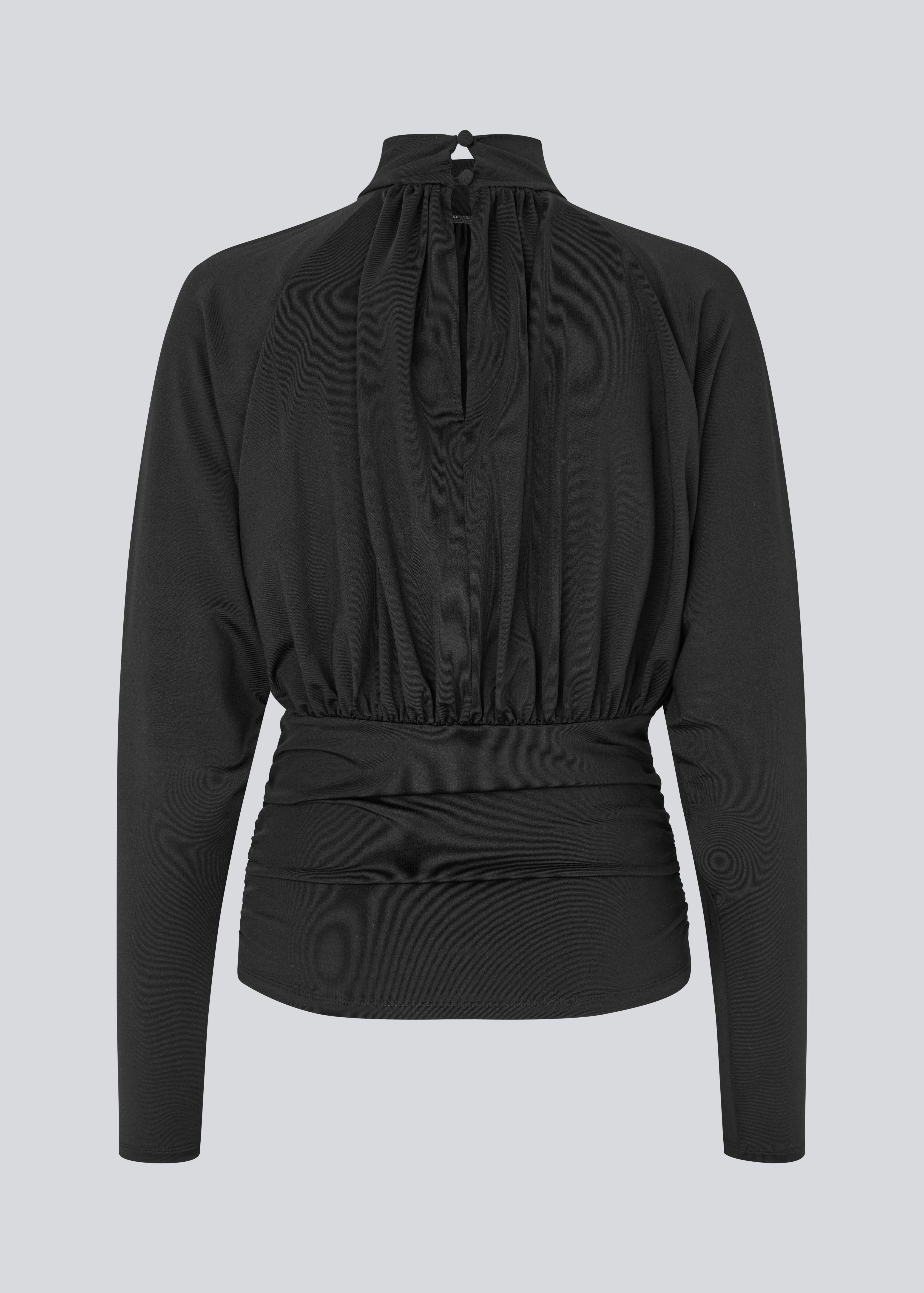 Elegant sort bluse med høj hals og lange ærmer. Blusen er designet med fine rynkedetaljer ved brystet og taljen, som skaber en flatterende silhuet. Den har en diskret knaplukning bagpå i nakken, som giver et sofistikeret og feminint udtryk. Det strækbare stof sikrer en behagelig pasform, mens det draperede snit tilføjer ekstra elegance. Perfekt til både hverdagsbrug og festlige lejligheder.