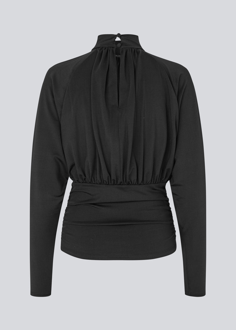 Elegant sort bluse med høj hals og lange ærmer. Blusen er designet med fine rynkedetaljer ved brystet og taljen, som skaber en flatterende silhuet. Den har en diskret knaplukning bagpå i nakken, som giver et sofistikeret og feminint udtryk. Det strækbare stof sikrer en behagelig pasform, mens det draperede snit tilføjer ekstra elegance. Perfekt til både hverdagsbrug og festlige lejligheder.