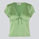 Feminin kortærmet top i glansfuld satin. AijaMD Top har fine detaljer som blondekanter, V-udskæring, let puf under brystet og sløjfedetalje. Fremstillet i 100% genanvendt polyester, perfekt til både elegante og afslappede looks.