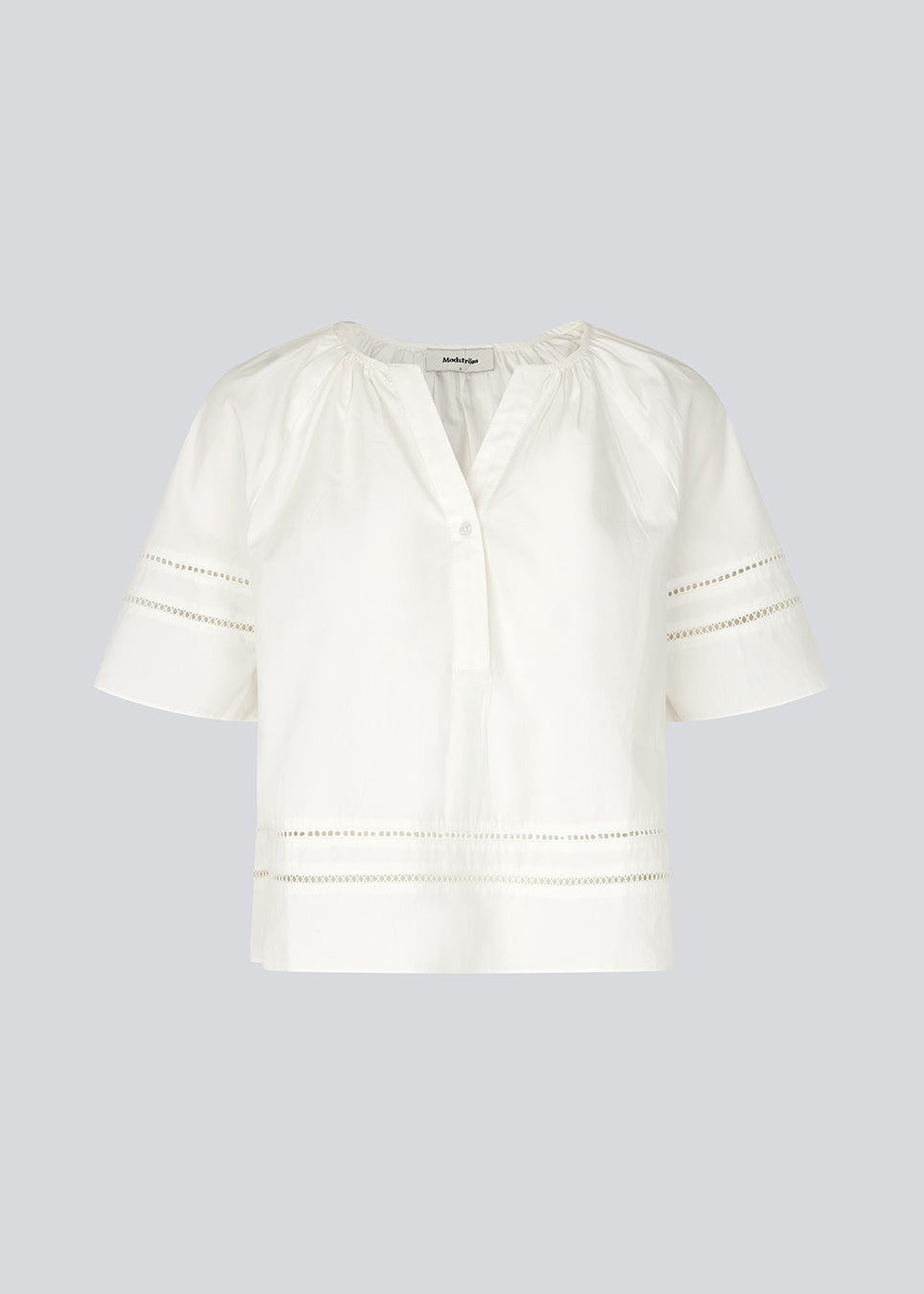 Kortærmet bluse med broderidetaljer. AyoMD Top har et løst snit og rynkedetaljer ved halsen samt V-udskæring med enkel knap. Toppen er fremstillet i et let materiale i 100% økologisk bomuld, perfekt til et feminint og afslappet look.