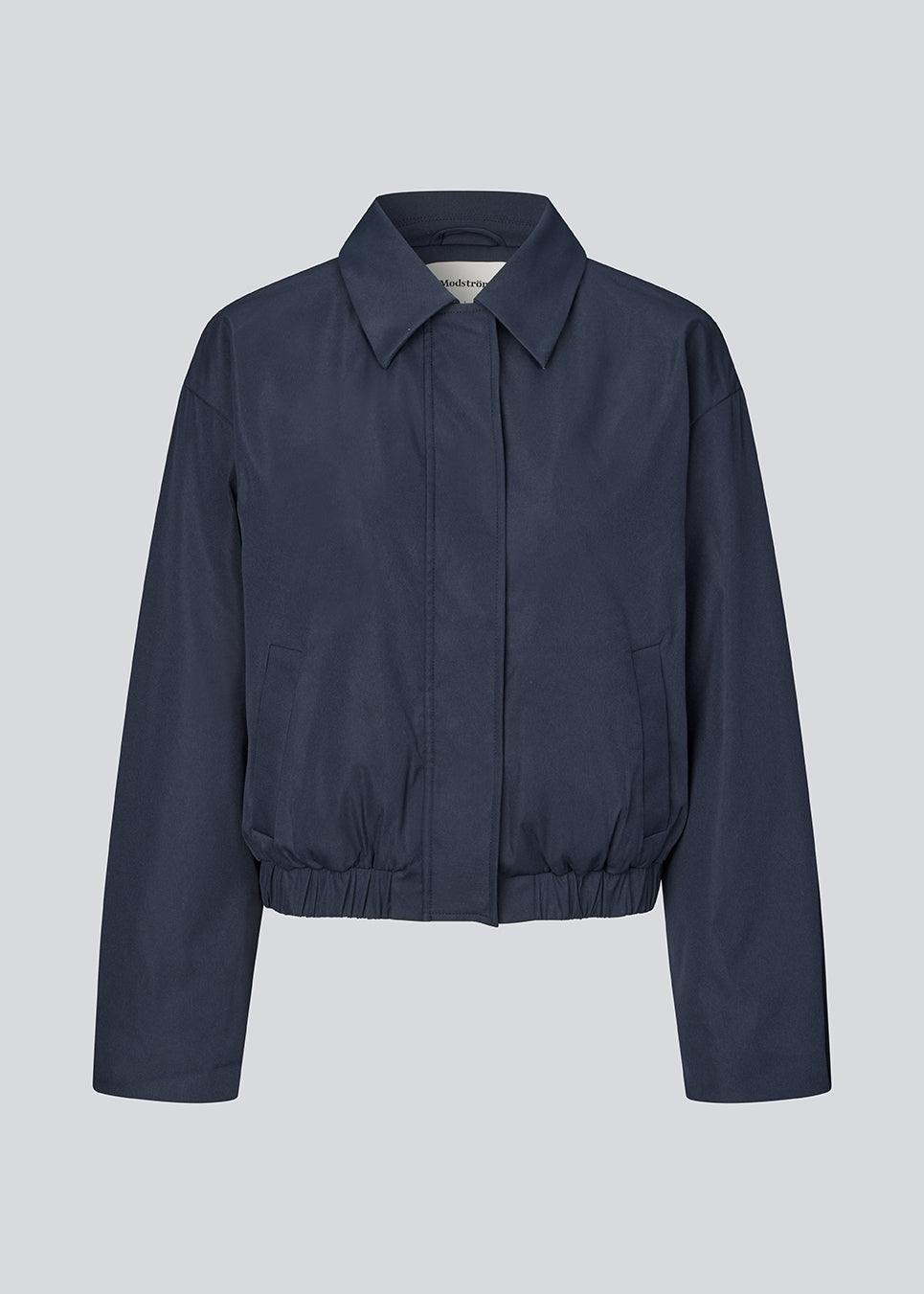Moderne og funktionel jakke. Badumd jacket er designet med klassisk krave, skjult lukning og elastisk kant, der skaber en afslappet, let cropped silhuet. En stilren overgangsjakke, der kombinerer et minimalistisk udtryk med komfort og alsidige stylingmuligheder.