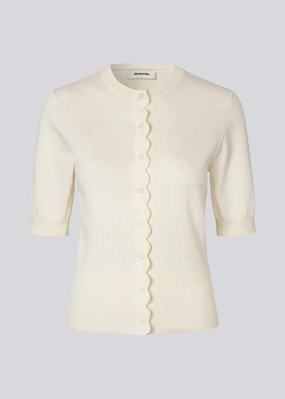 Feminin kortærmet cardigan i let strik. Bennamd SS Cardigan har klassiske detaljer som ribkanter, knappelukning og rund halsudskæring samt en fin bølgekant langs knappelukningen, der giver et elegant touch.&nbsp;