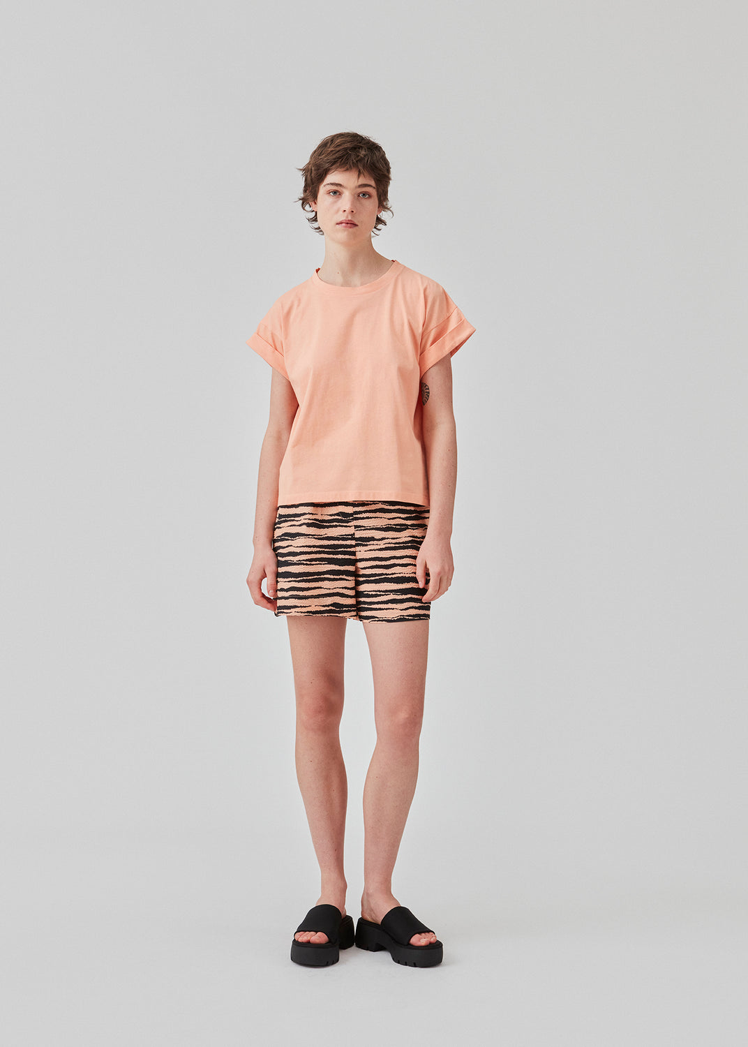 T-shirt i farven Peach Nectar i økologisk bomuld med en smule kortere længde. BrazilMD short t-shirt har rund hals og opsmøgede ærmer. Modellen er 177 cm og har en størrelse S/36 på.