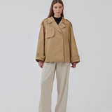 Populær kort trenchcoat i beige i bomuldskvalitet med skjult knaplukning fortil. Clara jacket har en oversize silhuet og klassiske detaljer. Med for. Modellen er 177 cm og har en størrelse S/36 på.