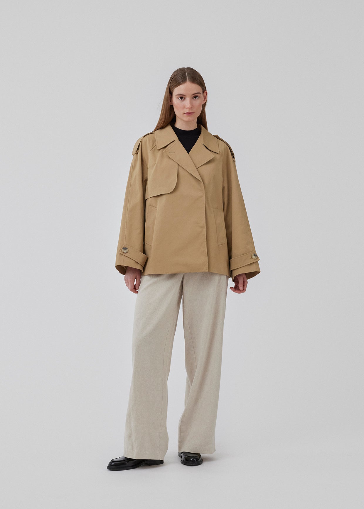 Populær kort trenchcoat i beige i bomuldskvalitet med skjult knaplukning fortil. Clara jacket har en oversize silhuet og klassiske detaljer. Med for. Modellen er 177 cm og har en størrelse S/36 på.