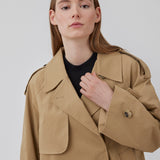 Populær kort trenchcoat i beige i bomuldskvalitet med skjult knaplukning fortil. Clara jacket har en oversize silhuet og klassiske detaljer. Med for. Modellen er 177 cm og har en størrelse S/36 på.
