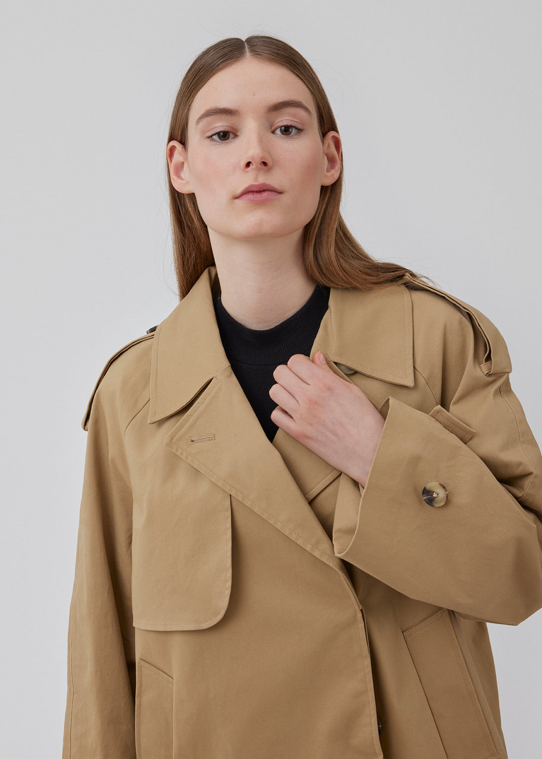 Populær kort trenchcoat i beige i bomuldskvalitet med skjult knaplukning fortil. Clara jacket har en oversize silhuet og klassiske detaljer. Med for. Modellen er 177 cm og har en størrelse S/36 på.