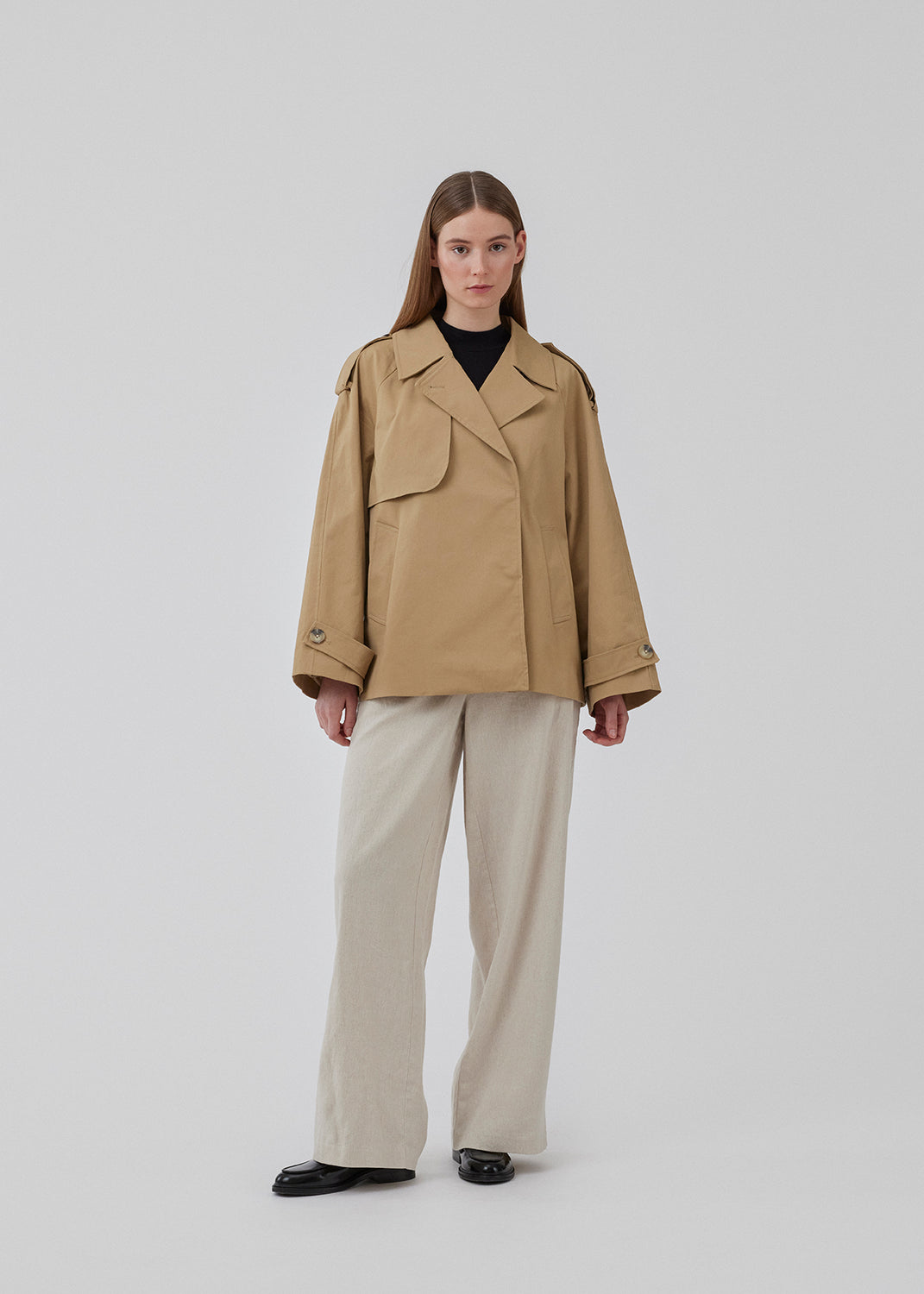 Populær kort trenchcoat i beige i bomuldskvalitet med skjult knaplukning fortil. Clara jacket har en oversize silhuet og klassiske detaljer. Med for. Modellen er 177 cm og har en størrelse S/36 på.