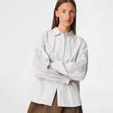 ColumbusMD Shirt er en skjorte med løs pasform og klassisk krave. Designet har gennemgående knaplukning, lange ærmer med manchetter og dekorative blomsterdetaljer langs ærmerne. Style den med jeans eller et par klassiske bukser til et enkelt hverdagslook. Modellen er 175 cm høj og bruger størrelse S/36.
 