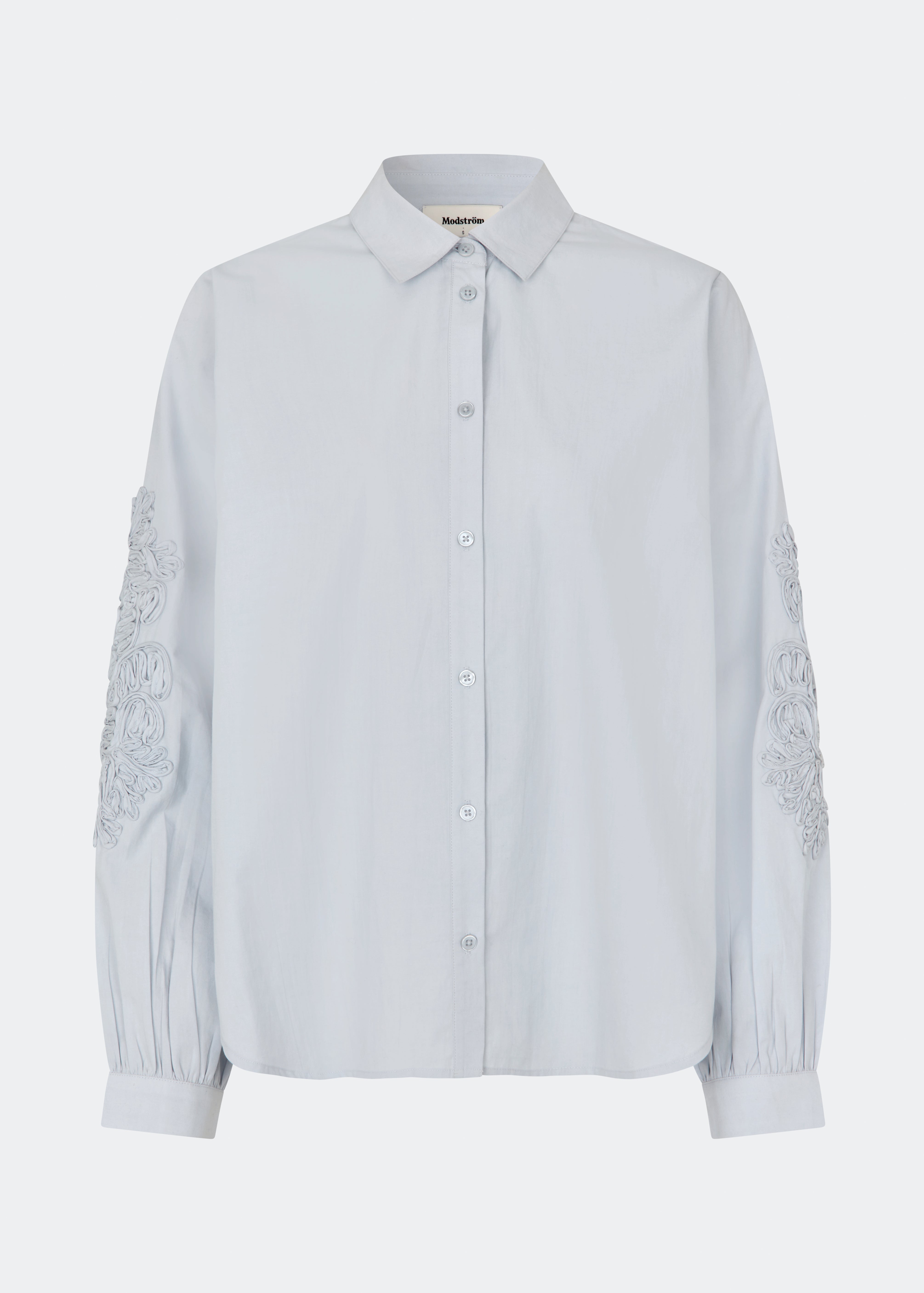 ColumbusMD Shirt er en skjorte med løs pasform og klassisk krave. Designet har gennemgående knaplukning, lange ærmer med manchetter og dekorative blomsterdetaljer langs ærmerne. Style den med jeans eller et par klassiske bukser til et enkelt hverdagslook. Modellen er 175 cm høj og bruger størrelse S/36.