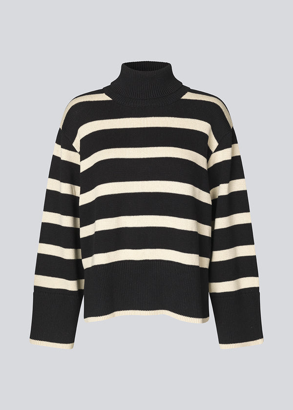Finstrikket, oversized trøje i bomuldsstrik i sort med beige striber. CorbinMD stripe t-neck har en ribstrikket rullekrave, lange brede ærmer og brede ribkanter ved ærmer og forneden. Modellen er 177 cm og har en størrelse S/36 på.