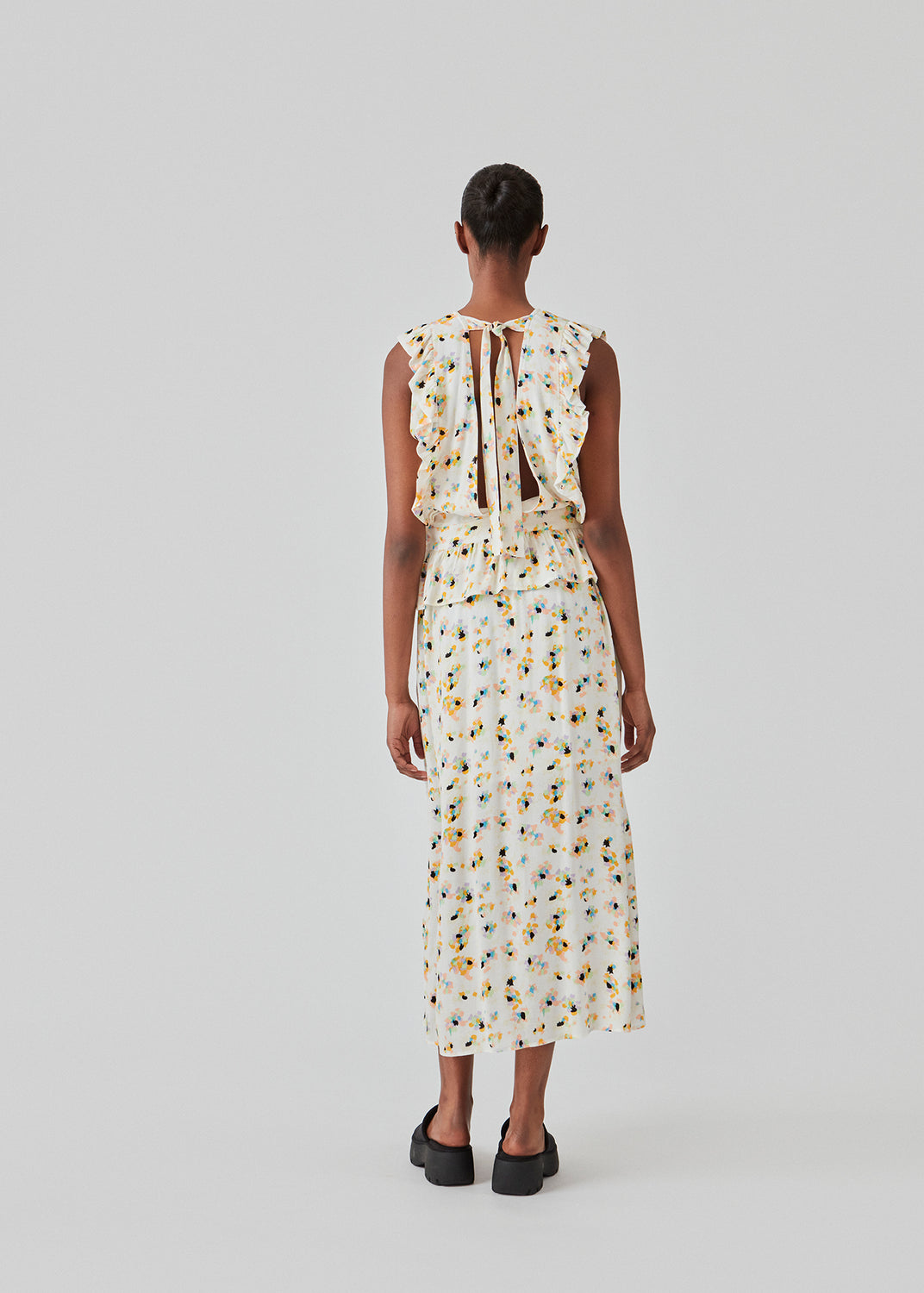 Ærmeløs top i farven Flower Sparkles med høj hals og let peplum-effekt. DafneMD print top har flæsedetaljer ned over skuldrene og forneden, samt åbning i ryggen med bindebånd. Modellen er 177 cm og har en størrelse S/36 på.
