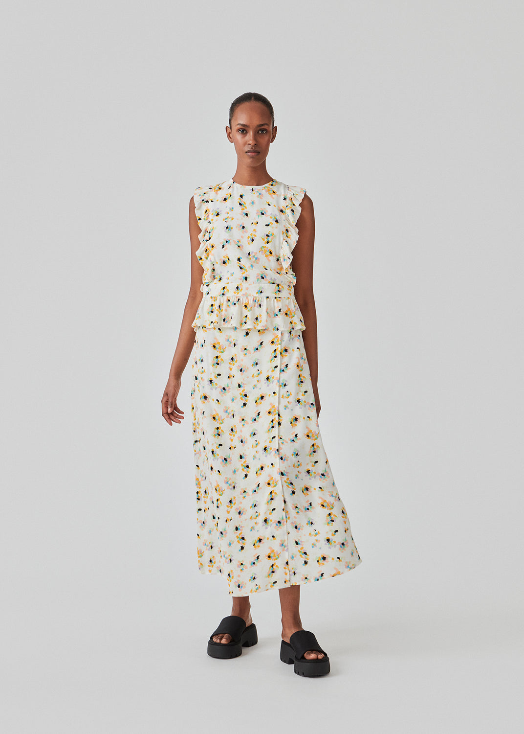 Ærmeløs top i farven Flower Sparkles med høj hals og let peplum-effekt. DafneMD print top har flæsedetaljer ned over skuldrene og forneden, samt åbning i ryggen med bindebånd. Modellen er 177 cm og har en størrelse S/36 på.