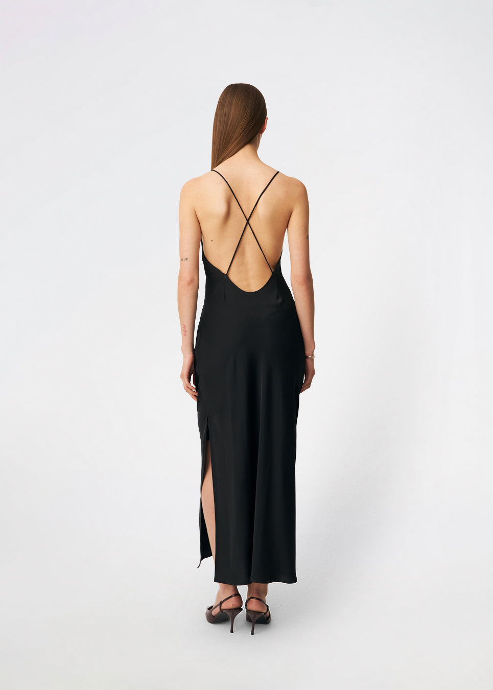 DanillaMD Dress er en lang satin-kjole med en elegant, figurnær silhuet. Designet har en lige halsudskæring, tynde stropper og draperede detaljer i siden, som skaber et blødt fald. Den åbne ryg med fine krydsende stropper tilfører et feminint udtryk. Style den med hæle og enkle accessories til særlige anledninger. Modellen er 175 cm høj og bruger størrelse S/36.