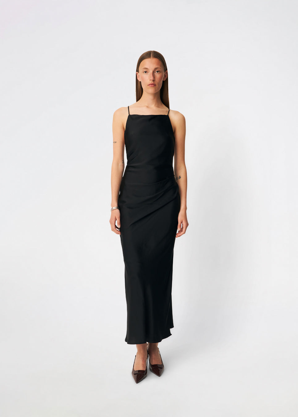 DanillaMD Dress er en lang satin-kjole med en elegant, figurnær silhuet. Designet har en lige halsudskæring, tynde stropper og draperede detaljer i siden, som skaber et blødt fald. Den åbne ryg med fine krydsende stropper tilfører et feminint udtryk. Style den med hæle og enkle accessories til særlige anledninger. Modellen er 175 cm høj og bruger størrelse S/36.