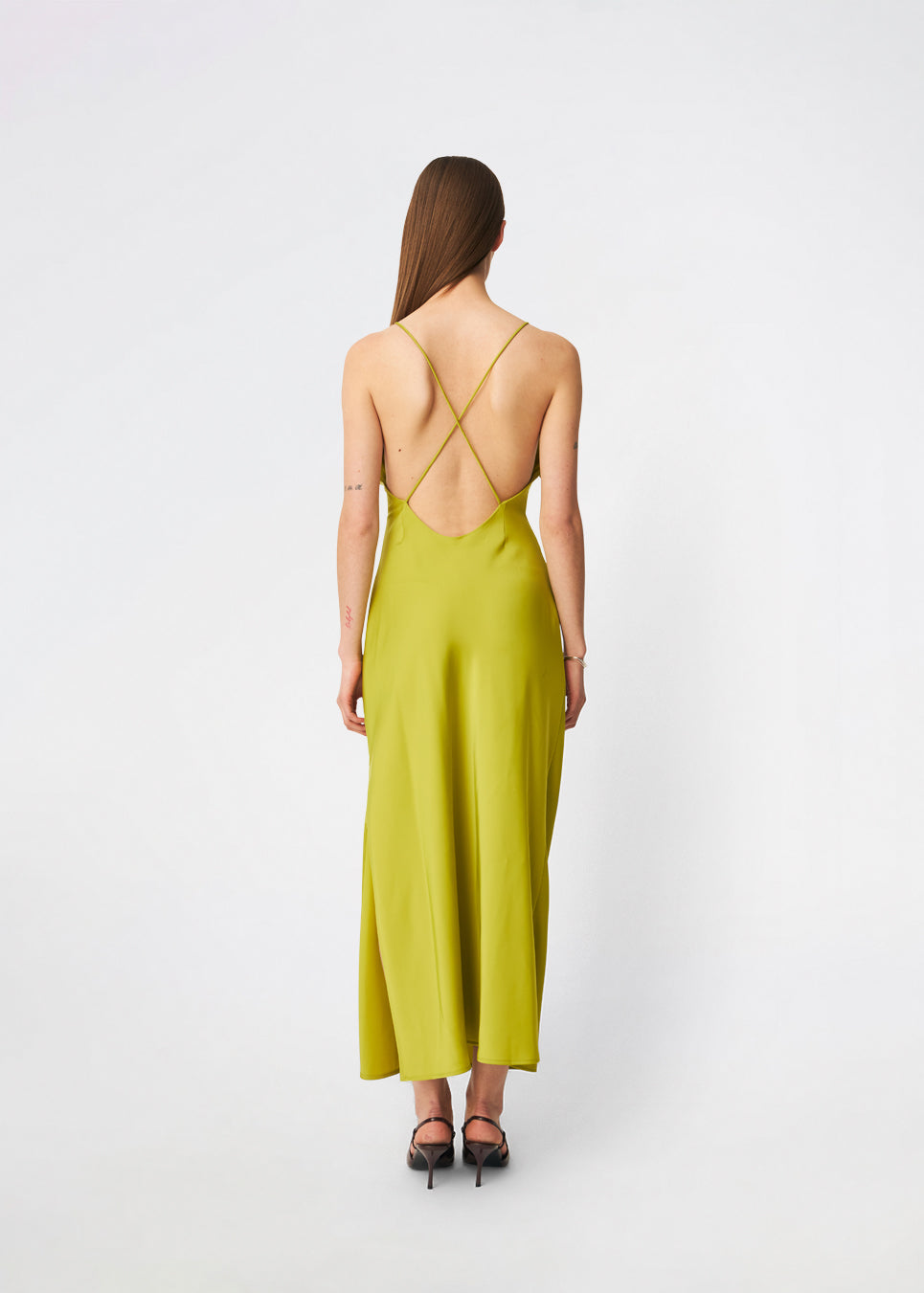DanillaMD Dress er en lang satin-kjole med en elegant, figurnær silhuet. Designet har en lige halsudskæring, tynde stropper og draperede detaljer i siden, som skaber et blødt fald. Den åbne ryg med fine krydsende stropper tilfører et feminint udtryk. Style den med hæle og enkle accessories til særlige anledninger. Modellen er 175 cm høj og bruger størrelse S/36.