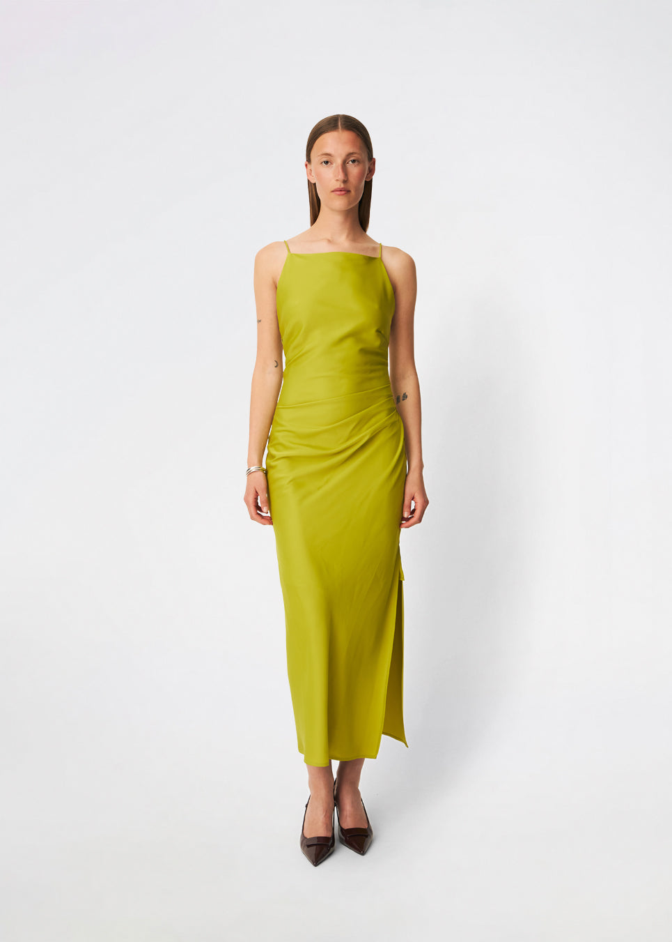 DanillaMD Dress er en lang satin-kjole med en elegant, figurnær silhuet. Designet har en lige halsudskæring, tynde stropper og draperede detaljer i siden, som skaber et blødt fald. Den åbne ryg med fine krydsende stropper tilfører et feminint udtryk. Style den med hæle og enkle accessories til særlige anledninger. Modellen er 175 cm høj og bruger størrelse S/36.
