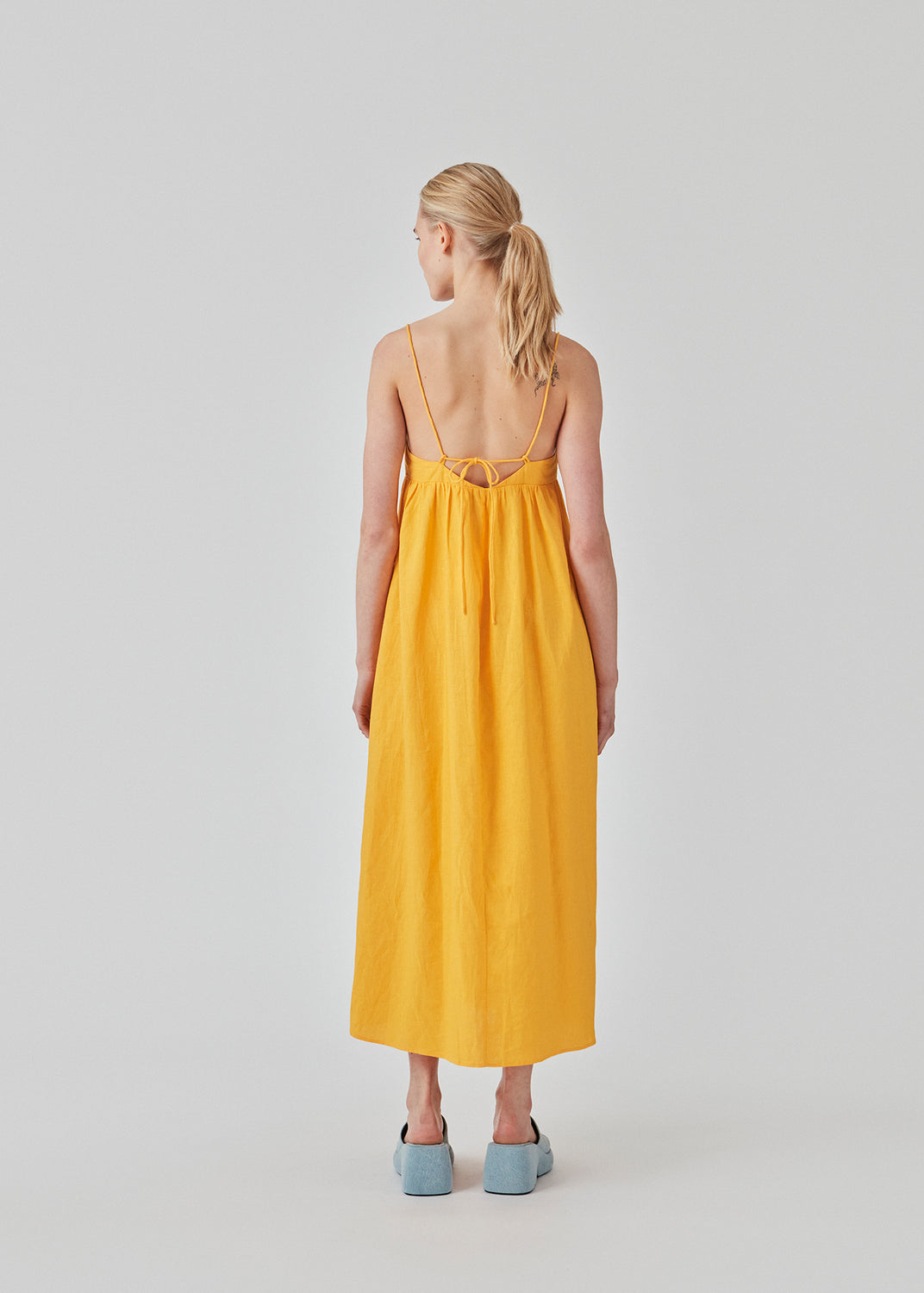 DarrelMD long dress i gul er designet i et hør mix med en tætsiddende top med v-udskæring, spaghettistropper med justerbart bindebånd bagpå og løst skørt. Med for. Modellen er 177 cm og har en størrelse S/36 på.