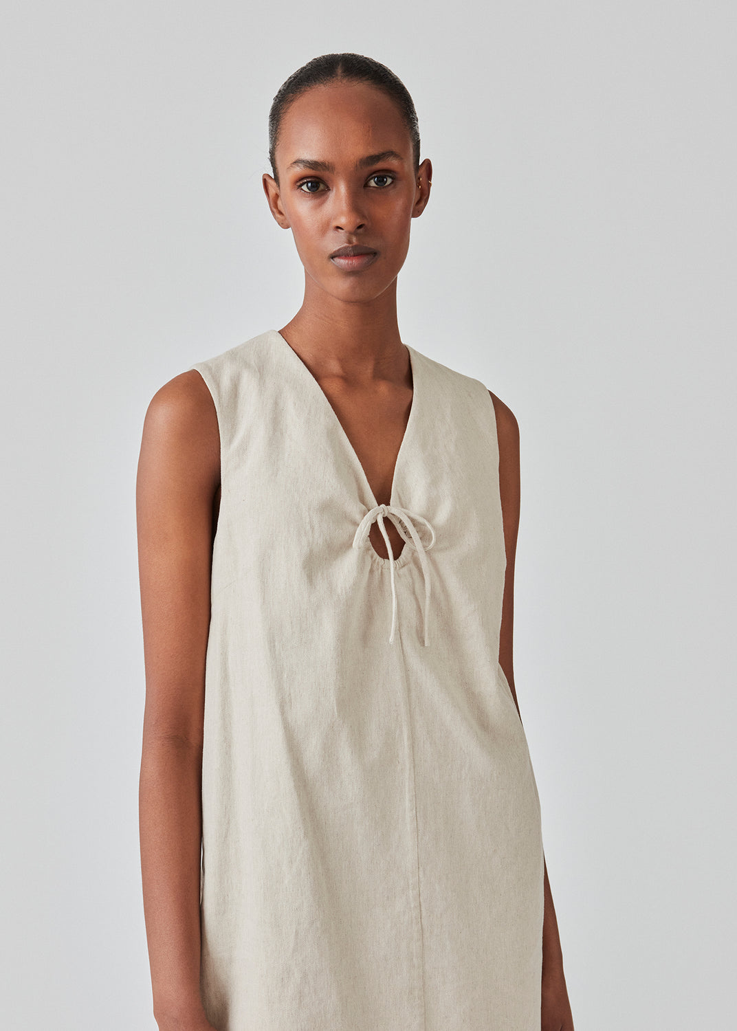 Kort kjole i hørkvalitet med A-facon. DaynaMD dress er uden ærmer, med dyb v-udskæring med cut out-detalje og bindebånd. Modellen er 177 cm og har en størrelse S/36 på.