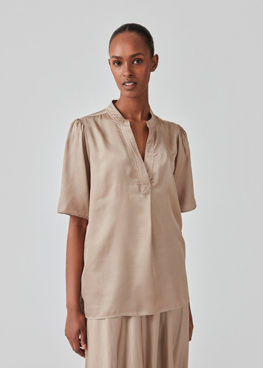 Beige bluse i satinkvalitet med afslappet pasform. DevanMD top har v-hals med åben krave og korte pufærmer. Modellen er 177 cm og har en størrelse S/36 på.