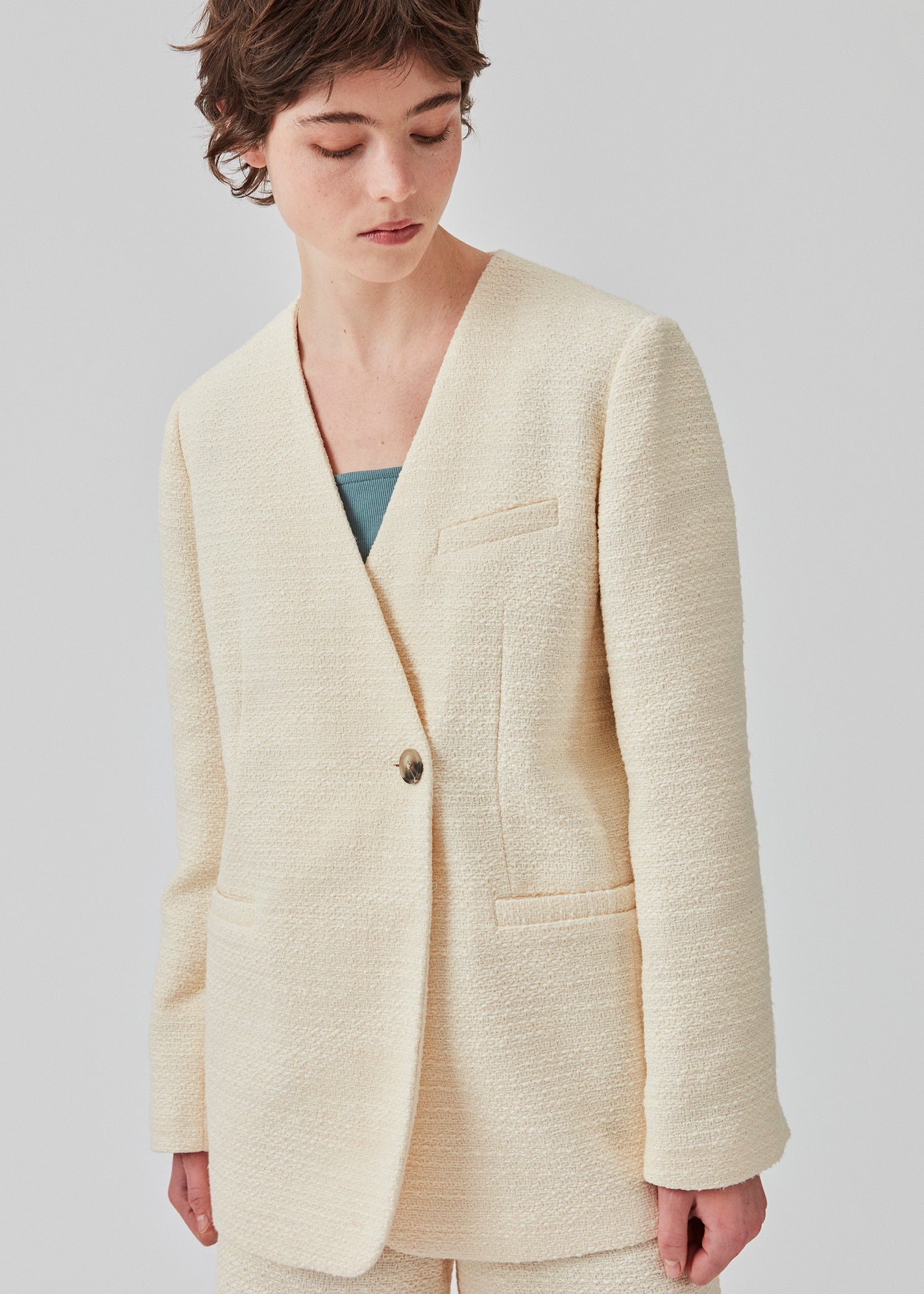 DimeMD blazer er designet i et tekstureret bomuldsmix med foer. Blazeren er uden krave og revers, men har en asymmetrisk wrap-detalje med en enkelt synlig knap. Modellen er 177 cm og har en størrelse S/36 på.  Style blazeren med matchende shorts: DimeMD shorts.