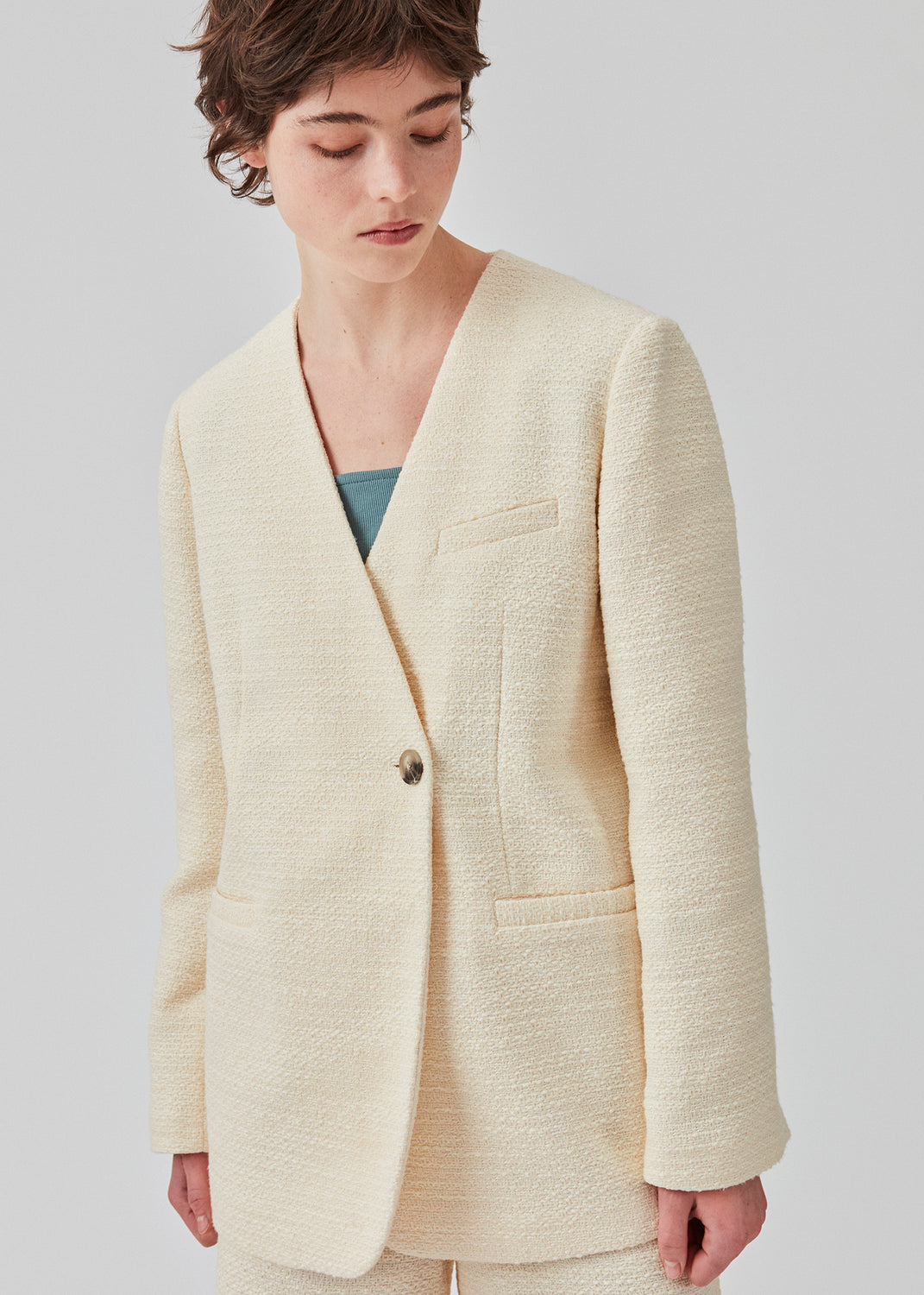 DimeMD blazer er designet i et tekstureret bomuldsmix med foer. Blazeren er uden krave og revers, men har en asymmetrisk wrap-detalje med en enkelt synlig knap. Modellen er 177 cm og har en størrelse S/36 på.  Style blazeren med matchende shorts: DimeMD shorts.