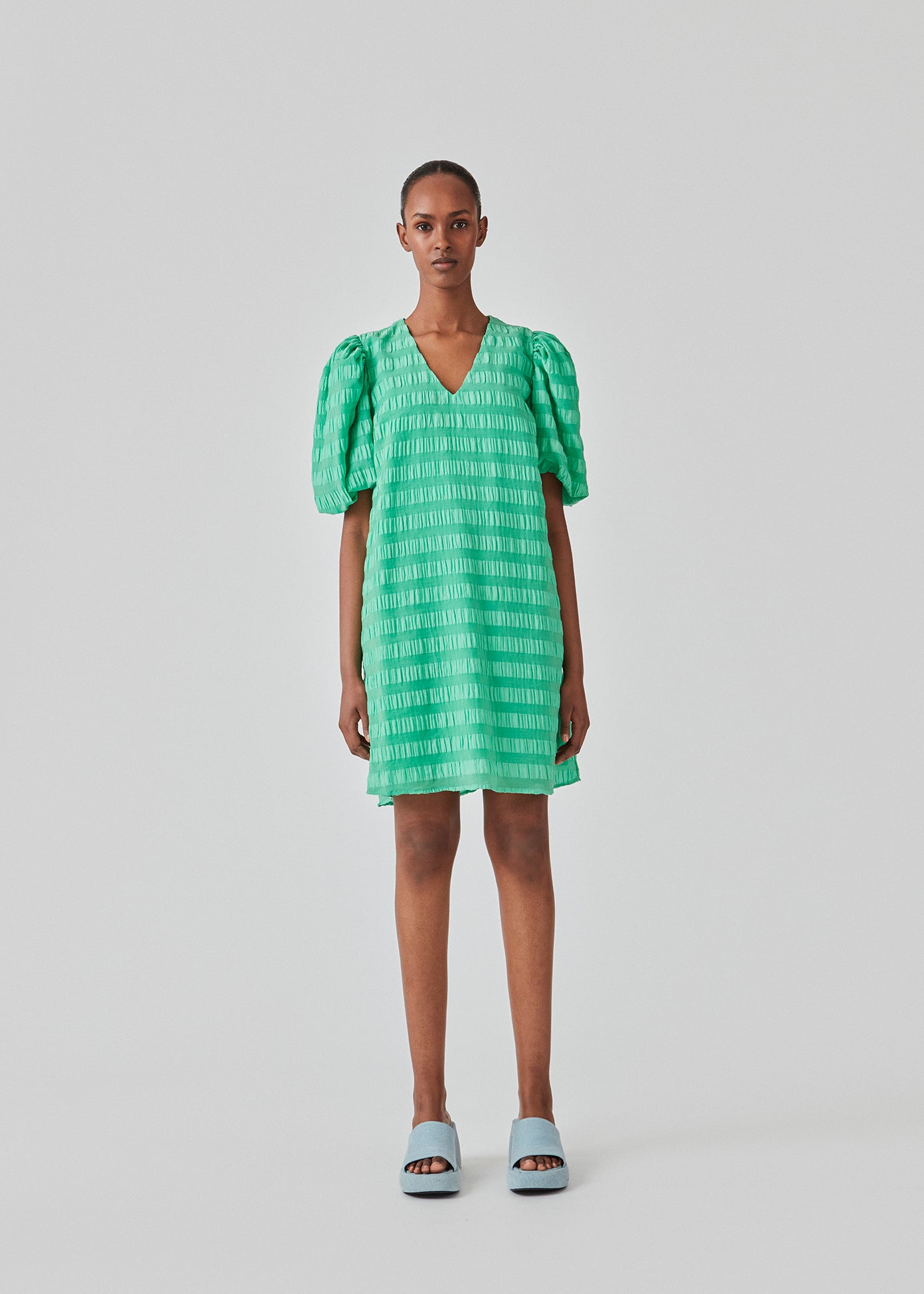 Kort kjole i grøn designet i et bæk og bølge materiale. DinoMD dress har v-udskæring i halsen, en løs pasform og korte puffærmer med elastik. Modellen er 177 cm og har en størrelse S/36 på.