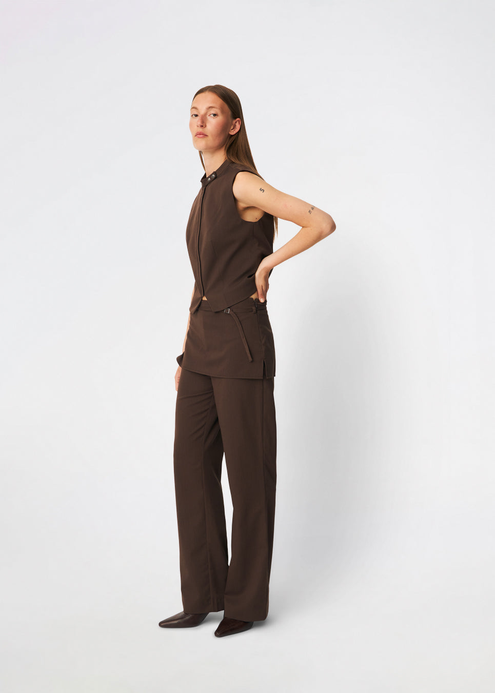 Dodomd Top er en elegant, ærmeløs top med en skarp silhuet og et moderne udtryk. Den høje hals med dekorative trykknapper og den skjulte frontlukning giver et rent, minimalistisk look, mens de figurskabende sømme fremhæver pasformen. Style den alene eller sammen med de matchende bukser for et sofistikeret sæt.