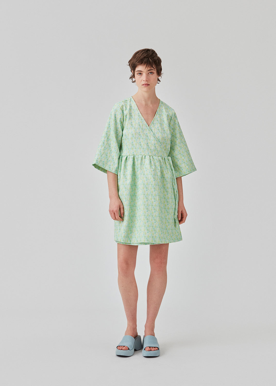 Kort kjole i struktureret materiale. DorianMD wrap dress har v-halsudskæring, brede ærmer i albuelængde og bindelukning. Modellen er 177 cm og har en størrelse S/36 på.