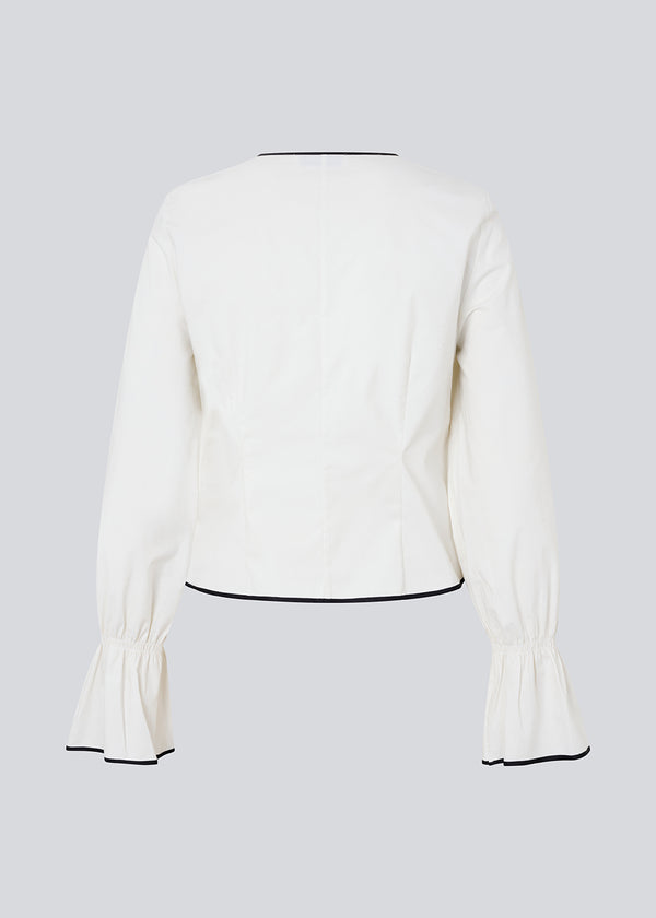 Figursyet top i hvid med lange løse ærmer. EmiliaMD bow shirt lukkes med tre sorte bindebånd foran og har en rynkedetalje ved håndleddet.<br>