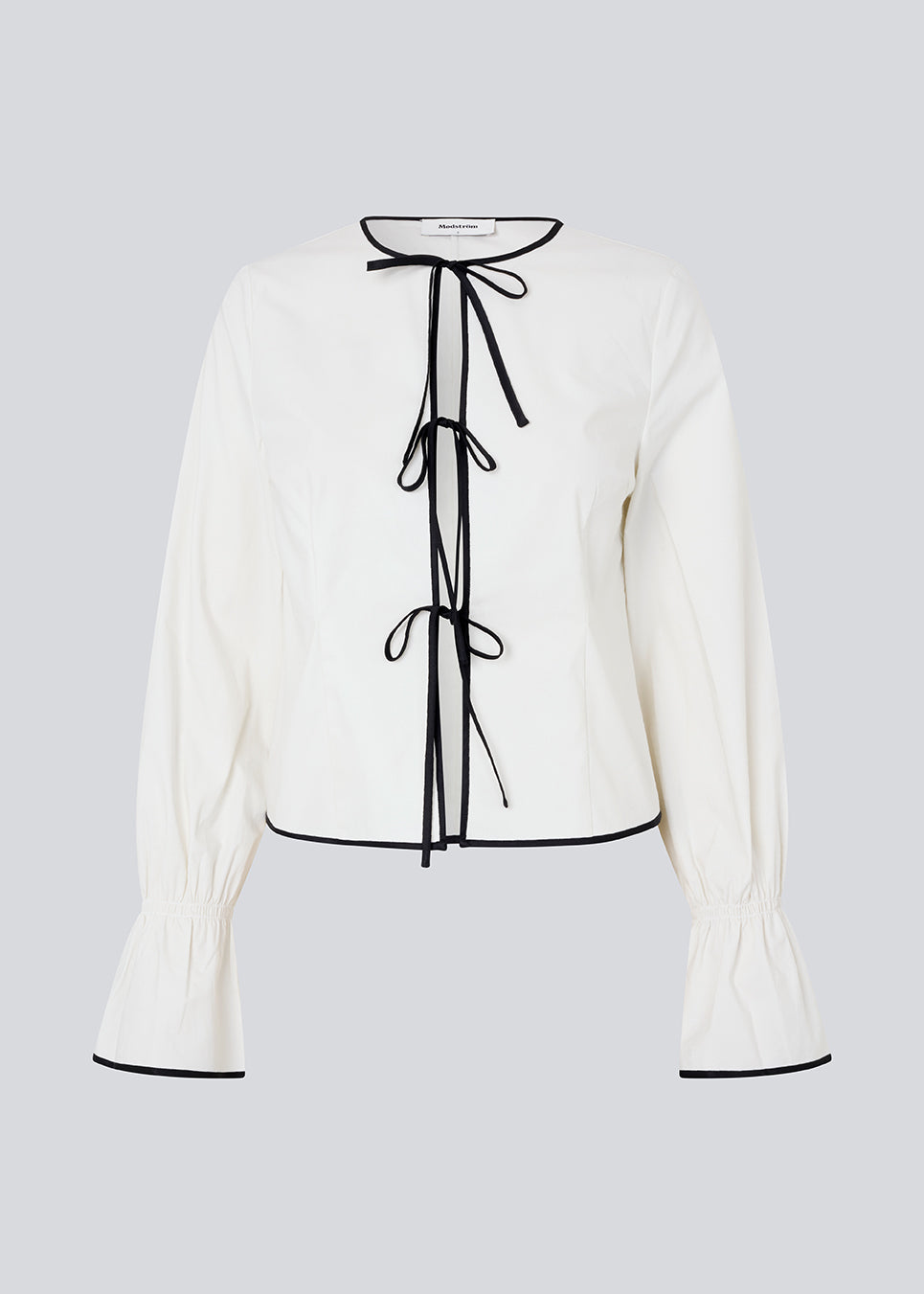 Figursyet top i hvid med lange løse ærmer. EmiliaMD bow shirt lukkes med tre sorte bindebånd foran og har en rynkedetalje ved håndleddet.<br>