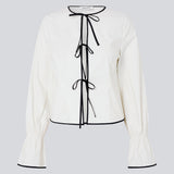 Figursyet top i hvid med lange løse ærmer. EmiliaMD bow shirt lukkes med tre sorte bindebånd foran og har en rynkedetalje ved håndleddet.<br>